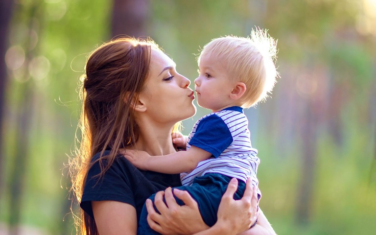 Eine junge Mutter will ihrem kleinen Sohn einen Kuss geben.