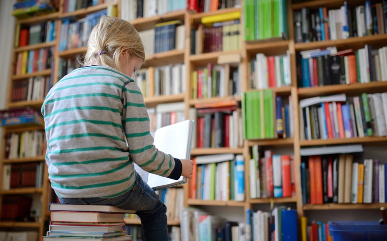 Ein Kind sitzt auf einem Buchstapel und liest ein Buch