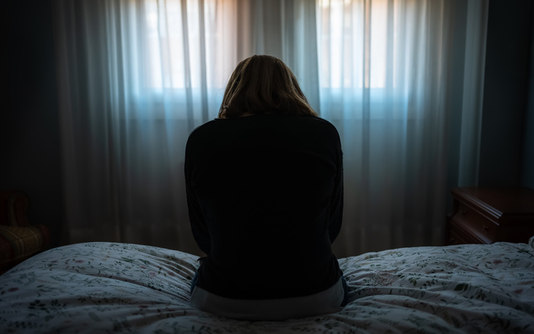 Frau sitzt auf dem Bett auf dem Rücken mit einer depressiven und müden Haltung