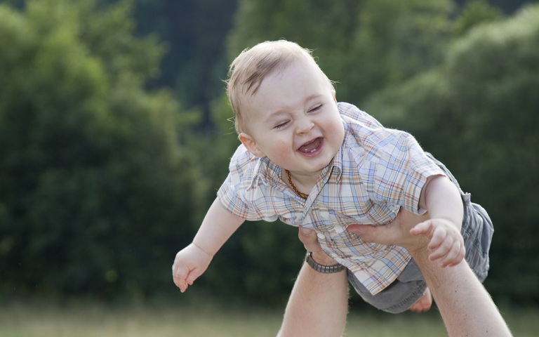 Vater mit seinem 9 Monate alten Sohn auf der Wiese, wirft ihn in die Luft