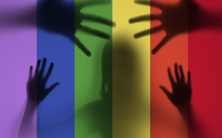 Schatten eines Kindes hinter Glasfassade aus Regenbogenfarben