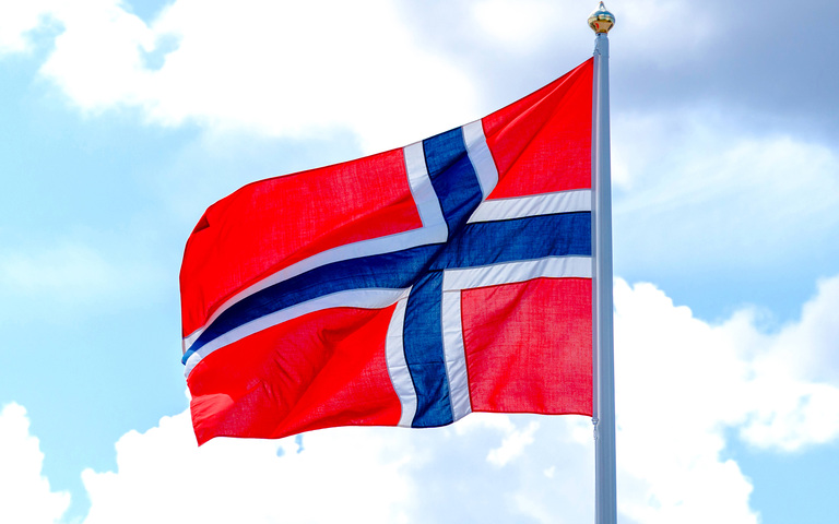 Eine norwegische Flagge weht im Wind vor einem blauen Himmel mit weißen Wolken.