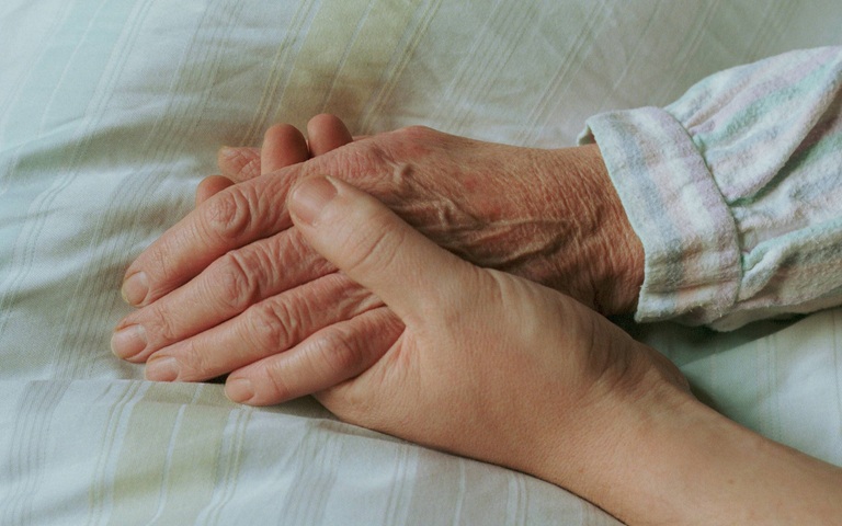 Einer alten Frau wird im Bett die Hand gehalten 