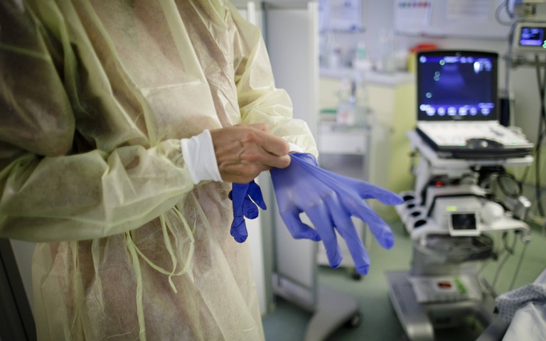 Eine Aerztin zieht sich blaue Handschuhe in einer Intensivstation an.